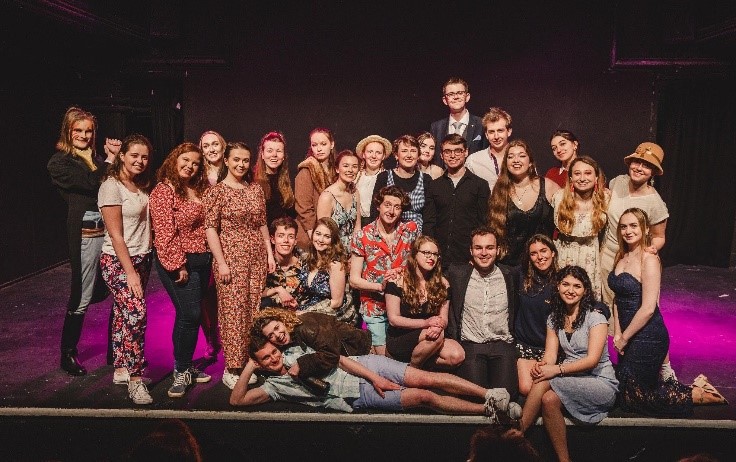 A photograph of Fionnuala with friends form a university society. They are stood on a stage lit with purple lighting.
