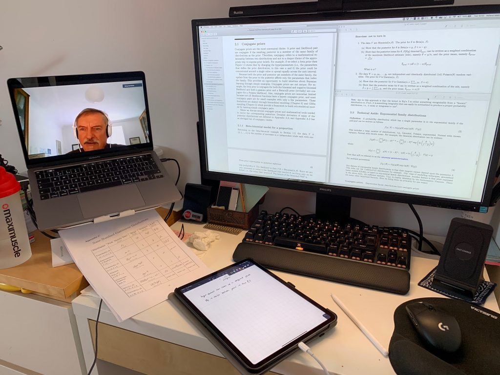 Photograph of Azfarul's work set up. On the left is a laptop showing the lecturer speaking, and on the right is a computer monitor showing the lecture notes. On the desk are written notes as well as a tablet.